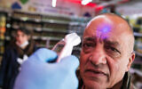 A security guard check the temperature of a customer to identify if he has a fever in a  Rami Levy supermarket in Jerusalem on  March 18, 2020. (Olivier Fitoussi/FLASH90)