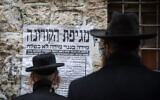Ultra Orthodox Jewish men look at a "Pashkvil"- information poster about the Coronavirus in Jerusalem on March 18, 2020. (Yonatan Sindel/Flash90 )