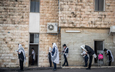 Jewish men pray outside a synagogue while maintaining social distancing as part of the campaign against the coronavirus outbreak, in Bayit Vegan, Jerusalem, on March 22, 2020. (Yonatan Sindel/Flash90)