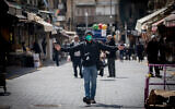 A photojournalist wears face mask and gloves for fear of the coronavirus at the Mahane Yehuda Market in Jerusalem on March 22, 2020. (Yonatan Sindel/Flash90)