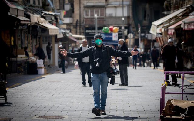 A photojournalist wears face mask and gloves for fear of the coronavirus at the Mahane Yehuda Market in Jerusalem on March 22, 2020. (Yonatan Sindel/Flash90) A photojournalist wears face mask and gloves for fear of the coronavirus at the Mahane Yehuda Market in Jerusalem on March 22, 2020. (Yonatan Sindel/Flash90)