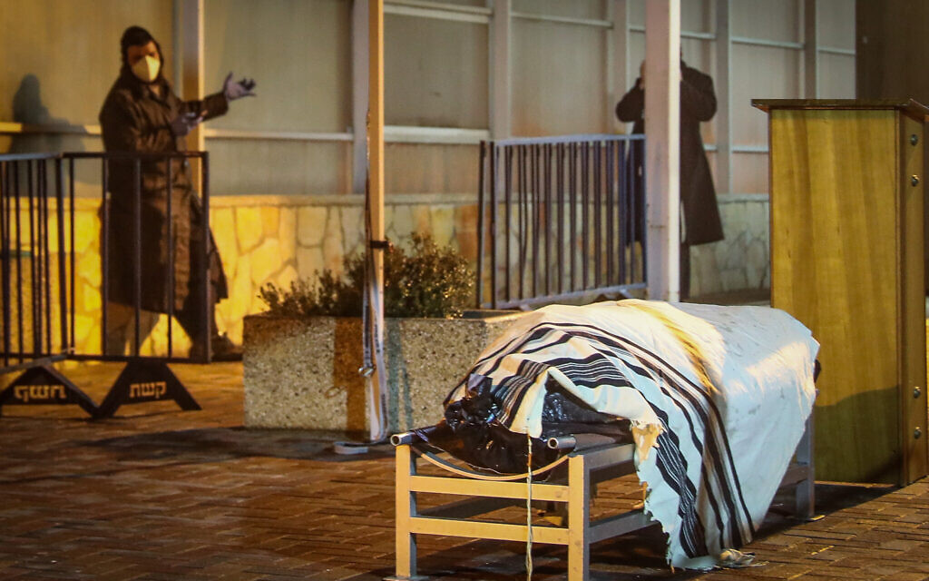 A man stands near the body of Holocaust survivor Aryeh Even, 88, the first man to die in Israel from the coronavirus epidemic, at the Har HaMenuchot Cemetery in Jerusalem, early on March 22, 2020. (Yonatan Sindel/Flash90) A man stands near the body of Holocaust survivor Aryeh Even, 88, the first man to die in Israel from the coronavirus epidemic, at the Har HaMenuchot Cemetery in Jerusalem, early on March 22, 2020. (Yonatan Sindel/Flash90)