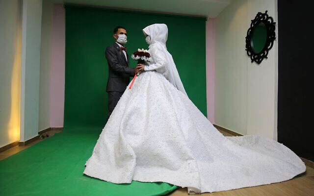Palestinian groom Mohamed abu Daga and his bride Israa wear face masks amid the novel coronavirus epidemic, during a photoshoot at a studio before their wedding ceremony in Khan Yunis in the southern Gaza Strip, on March 23, 2020. (Abed Rahim Khatib/ Flash90) Palestinian groom Mohamed abu Daga and his bride Israa wear face masks amid the novel coronavirus epidemic, during a photoshoot at a studio before their wedding ceremony in Khan Yunis in the southern Gaza Strip, on March 23, 2020. (Abed Rahim Khatib/ Flash90)