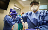 Medical personnel wearing protective gear handle a coronavirus test sample at Hadassah Hospital Ein Kerem in Jerusalem on March 24, 2020 (Yossi Zamir/Flash90)