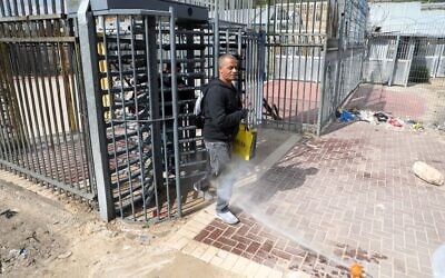 Palestinian health workers disinfect Palestinian laborers as they cross back from Israel at a checkpoint in Tarqumiya on March 25, 2020 (Wisam Hashlamoun/Flash90)