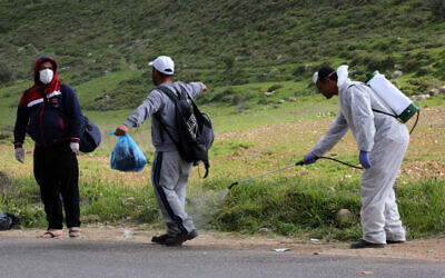 Palestinian health workers disinfectant Palestinian workers as they cross back from Israel at a checkpoint in Tarqumiya on March 25, 2020. (Wisam Hashlamoun/Flash90)