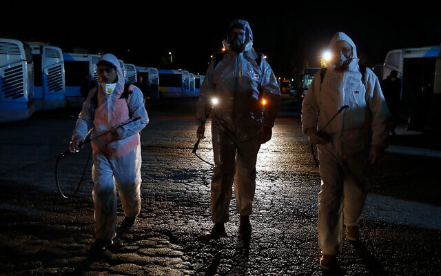 Workers wearing protective suits at a bus depot before they spray disinfectant inside the vehicles in Athens, March 14, 2020. (AP Photo/Thanassis Stavrakis) Workers wearing protective suits at a bus depot before they spray disinfectant inside the vehicles in Athens, March 14, 2020. (AP Photo/Thanassis Stavrakis)