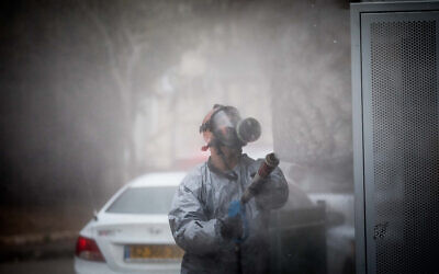 An Israeli firefighter wearing protective clothes disinfects a bus station in the ultra-Orthodox town of Kiryat Ye'arim (Telz-Stone) after seventeen of the city's residents were found to have coronavirus, March 18, 2020. (Yonatan Sindel/Flash90)