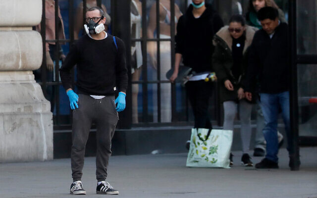 A man wearing a mask waits with other people at a bus stop in London, March 24, 2020. (AP Photo/Frank Augstein) A man wearing a mask waits with other people at a bus stop in London, March 24, 2020. (AP Photo/Frank Augstein)