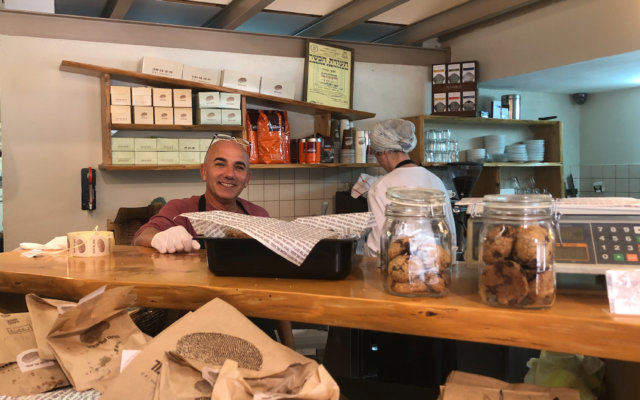 Nissim Naveh mans the counter at the Lechem shel Tomer in Arnona, where customers lined up to buy bread but couldn't sit to drink coffee on March 15, 2020 (Jessica Steinberg/Times of Israel)