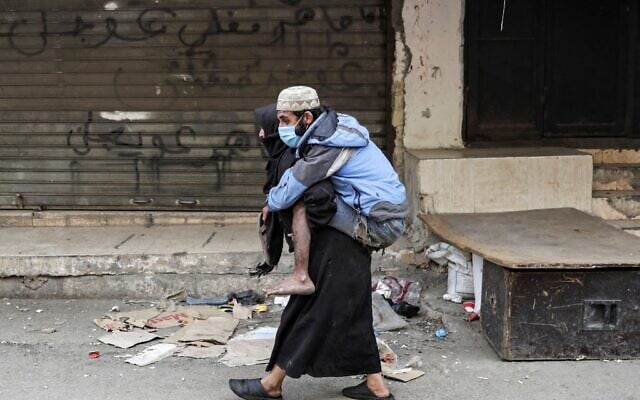 A woman carries a diabled man wearing a protective face mask the Sabra neighbourhood of Beirut where many Palestinian refugees still live on March 22, 2020. (ANWAR AMRO / AFP) A woman carries a diabled man wearing a protective face mask the Sabra neighbourhood of Beirut where many Palestinian refugees still live on March 22, 2020. (ANWAR AMRO / AFP)