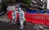 Workers wearing protective suits walk next to Huanan Seafood Wholesale Market in Wuhan, in China's central Hubei province on March 30, 2020, after travel restrictions into the city were eased following more than two months of lockdown due to the COVID-19 coronavirus outbreak. (Hector Retamal/AFP)