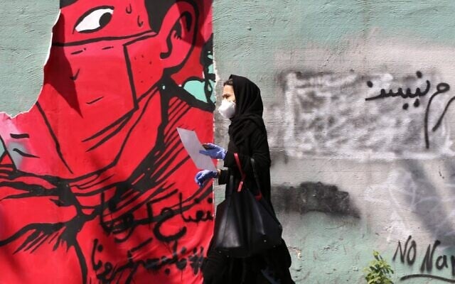 An Iranian woman wearing a protective mask and gloves walks past a mask graffiti in Tehran on April 13, 2020, during the coronavirus COVID-19 pandemic. (ATTA KENARE / AFP) An Iranian woman wearing a protective mask and gloves walks past a mask graffiti in Tehran on April 13, 2020, during the coronavirus COVID-19 pandemic. (ATTA KENARE / AFP)