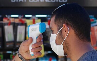 A worker checks the temperature of a customer before allowing him to enter a hardware store in Jerusalem on April 20, 2020, amid the coronavirus pandemic. (Emmanuel Dunand/AFP)