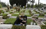 Israelis, wearing a protective mask against the coronavirus (COVID-19), pay their respects over the grave of a soldier at the Mount Herzl military cemetery in Jerusalem on April 26, 2020. (MENAHEM KAHANA / AFP)