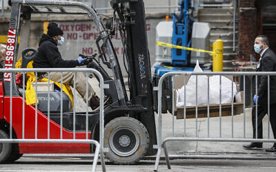 Bodies wrapped in plastic are loaded on to a refrigerated container truck operating as a makeshift morgue while being handled by medical workers wearing personal protective equipment due to COVID-19 concerns, Tuesday, March 31, 2020, at Brooklyn Hospital Center in the Brooklyn borough of New York. (AP Photo/John Minchillo)