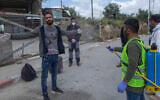 A paramedic from the Palestinian Authority Ministry of Health disinfects Palestinian laborers to help contain the coronavirus, as they exit an Israeli army checkpoint after returning from work in Israel, near the West Bank village of Nilin, west of Ramallah, April 7, 2020. (AP Photo/Nasser Nasser)