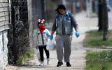 In this April 7, 2020 photo, Erica Harris, right, and her daughter Jordan, wear their protective masks as they walk back home after getting a lunch and homework from the child’s school on Chicago’s Southside in Chicago (AP Photo/Charles Rex Arbogast)