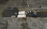 Workers wearing personal protective equipment bury bodies in a trench on Hart Island, Thursday, April 9, 2020, in the Bronx borough of New York. On Thursday, New York City’s medical examiner confirmed that the city has shortened the amount of time it will hold on to remains to 14 days from 30 days before they will be transferred for temporary internment at a City Cemetery.  (AP Photo/John Minchillo)