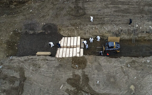 Workers wearing personal protective equipment bury bodies in a trench on Hart Island, Thursday, April 9, 2020, in the Bronx borough of New York. On Thursday, New York City’s medical examiner confirmed that the city has shortened the amount of time it will hold on to remains to 14 days from 30 days before they will be transferred for temporary internment at a City Cemetery. (AP Photo/John Minchillo) Workers wearing personal protective equipment bury bodies in a trench on Hart Island, Thursday, April 9, 2020, in the Bronx borough of New York. On Thursday, New York City’s medical examiner confirmed that the city has shortened the amount of time it will hold on to remains to 14 days from 30 days before they will be transferred for temporary internment at a City Cemetery. (AP Photo/John Minchillo)