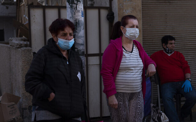 In this April 2, 2020, photo, people wear protective face masks to prevent the spread of the new coronavirus as they wait at food distribution center providing food products for families ahead of the upcoming Jewish holiday of Passover, in Tel Aviv, Israel. The once thrumming city of Tel Aviv, famed for its nightlife and bustling beachfront, has fallen eerily quiet due to Israel's tight movement restrictions to halt the spread of the coronavirus. (AP Photo/Oded Balilty)