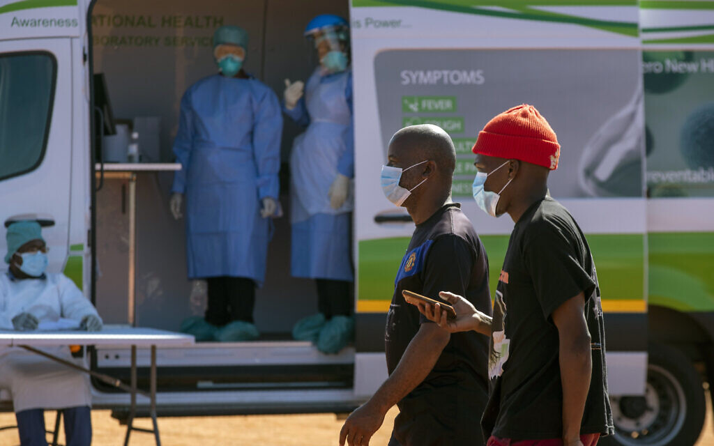Men walk past health workers in a mobile testing clinic to queue for screening and test for COVID-19 at Lenasia South, south Johannesburg, South Africa, April 21, 2020. (AP Photo/Themba Hadebe)