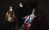 Illustrative: Travelers wearing protective masks arrive at Ben Gurion Airport, Feb. 27, 2020. (AP Photo/Ariel Schalit)