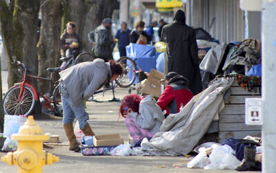 In this March 3, 2020, photo, homeless people crowd a sidewalk in downtown Salem, Oregon, where they have set up a makeshift camp. (AP Photo/Andrew Selsky)