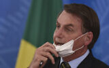 Brazil's President Jair Bolsonaro removes his mask to speak to journalists after a press conference on the new coronavirus, at the Planalto Presidential Palace in Brasilia, Brazil on March 18, 2019. (AP/Andre Borges)