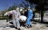 People wearing protective clothing carry the body of a victim who died after being infected with the new coronavirus at a cemetery just outside Tehran, Iran, Monday, March 30, 2020.  (AP Photo/Ebrahim Noroozi)