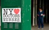 A sign acknowledging the work of doctors and nurses is posted on a traffic control box outside Brooklyn Hospital Center, as a hospital worker, right, waits for a traffic light to change before reporting to duty, Sunday, April 5, 2020, in New York. The Brooklyn hospital is one of several in the area treating high numbers of coronavirus patients. (AP Photo/Kathy Willens)