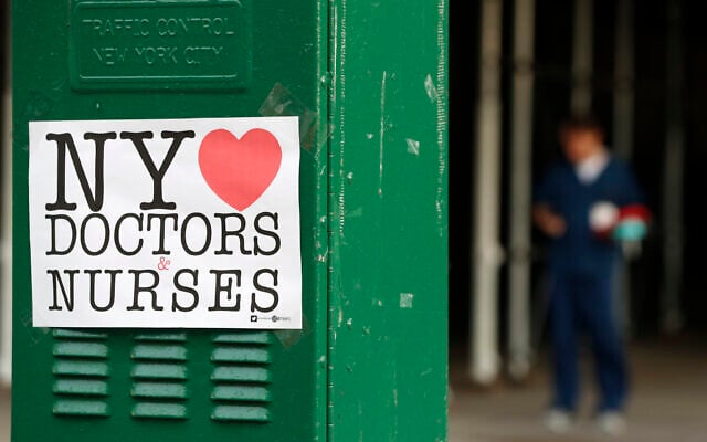 A sign acknowledging the work of doctors and nurses is posted on a traffic control box outside Brooklyn Hospital Center, as a hospital worker, right, waits for a traffic light to change before reporting to duty, Sunday, April 5, 2020, in New York. The Brooklyn hospital is one of several in the area treating high numbers of coronavirus patients. (AP Photo/Kathy Willens) A sign acknowledging the work of doctors and nurses is posted on a traffic control box outside Brooklyn Hospital Center, as a hospital worker, right, waits for a traffic light to change before reporting to duty, Sunday, April 5, 2020, in New York. The Brooklyn hospital is one of several in the area treating high numbers of coronavirus patients. (AP Photo/Kathy Willens)