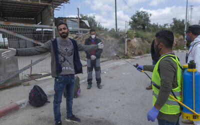 In this Tuesday, April 7, 2020 photo, a paramedic from the Palestinian Ministry of Health disinfects Palestinian laborers to help contain the coronavirus, as they exit an Israeli army checkpoint after returning from work in Israel, near the West Bank village of Nilin, west of Ramallah.  (AP/Nasser Nasser)