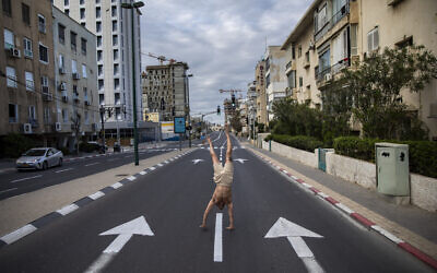 An Israeli man stands on his hands on an empty road during a lockdown following government measures to help stop the spread of the coronavirus, in Tel Aviv, April 8, 2020. (AP Photo/Oded Balilty)