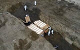 Workers wearing personal protective equipment bury bodies in a trench on Hart Island,  April 9, 2020, in the Bronx borough of New York amid the mounting death toll from the coronavirus outbreak. (AP Photo/John Minchillo)