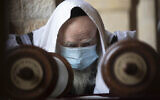 A Jewish man wears a face mask to curb the spread of the coronavirus as he reads from a Torah scroll at the Western Wall in the Jerusalem Old City, April 10, 2020. (AP Photo/Sebastian Scheiner)