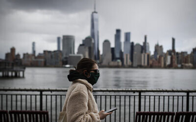 The downtown New York City skyline looms over pedestrians wearing masks due to COVID-19 concerns, Friday, April 10, 2020, in Jersey City, NJ (AP Photo/John Minchillo)