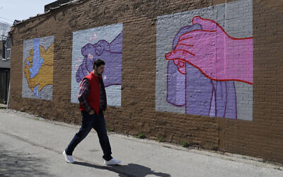 A man walks by a mural depicting hand washing in Logan Square by artist James Mosher, Saturday, April 11, 2020 in Chicago. (AP Photo/Nam Y. Huh)
