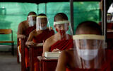 Novice Buddhist monks with protective masks and face shields, seated maintaining social distancing participate in a religious class at Molilokayaram Educational Institute in Bangkok, Thailand,  April 15, 2020. (AP Photo/Gemunu Amarasinghe)