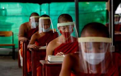 Novice Buddhist monks with protective masks and face shields, seated maintaining social distancing participate in a religious class at Molilokayaram Educational Institute in Bangkok, Thailand,  April 15, 2020. (AP Photo/Gemunu Amarasinghe)