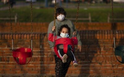 Illustrative: A child wearing a mask to prevent the spread of coronavirus is pushed in a swing by a woman in Montevideo, Uruguay, April 23, 2020.(AP Photo/Matilde Campodonico)