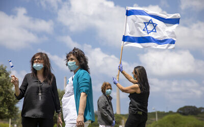 Medical staff and patients wear masks and wave Israeli flags as an Israeli Air Force aerobatic team flies in formation over the Hillel Yaffe Medical Center, in the northern city of Hadera, April 29, 2020. (Ariel Schalit/AP)
