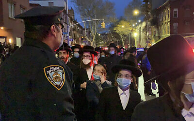 A New York City police officer keeps watch as hundreds of mourners gather in the Brooklyn borough of New York, Tuesday, April 28, 2020, to observe a funeral for Rabbi Chaim Mertz, a Hasidic Orthodox leader whose death was reportedly tied to the coronavirus. (Peter Gerber via AP)