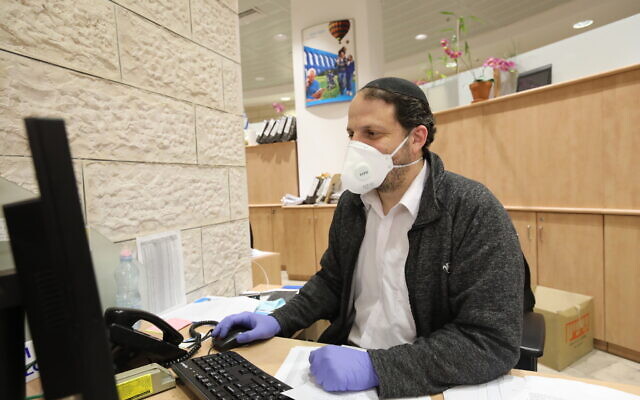 Illustrative: A bank teller wearing a face mask for fear of the coronavirus seen working in a bank in Jerusalem on March 17, 2020. (Yossi Zamir/Flash90 Illustrative: A bank teller wearing a face mask for fear of the coronavirus seen working in a bank in Jerusalem on March 17, 2020. (Yossi Zamir/Flash90