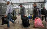Palestinian workers from the West Bank city of Hebron carry personal belongings as they arrive at the Tarqumiya checkpoint to cross into Israel on March 18, 2020. (Wisam Hashlamoun/Flash90)