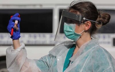 A health care worker at Hadassah Ein Kerem hospital holding a model of a coronavirus test kit, March 26, 2020. (Olivier Fitoussi/Flash90)