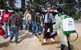 Palestinian health workers disinfectant Palestinian workers as they cross back from Israel to the West Bank at a checkpoint in Tarqumiya on March 27, 2020. (Wisam Hashlamoun/Flash90)
