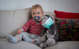 A baby girl plays with a masked monkey in Tel Aviv on March 29, 2020. (Miriam Alster/Flash90)