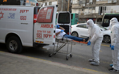 Magen David Adom paramedics in protective gear put a man suspected of having the coronavirus into an ambulance in the the Tel Aviv suburb of Bnei Brak, March 31, 2020. (Gili Yaari/Flash90)
