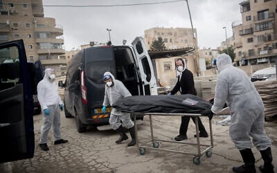 Workers wearing protective clothes carry the body of a patient who died from complications of coronavirus, at the Shamgar Funeral Home in Jerusalem on April 1, 2020 (Yonatan Sindel/Flash90)